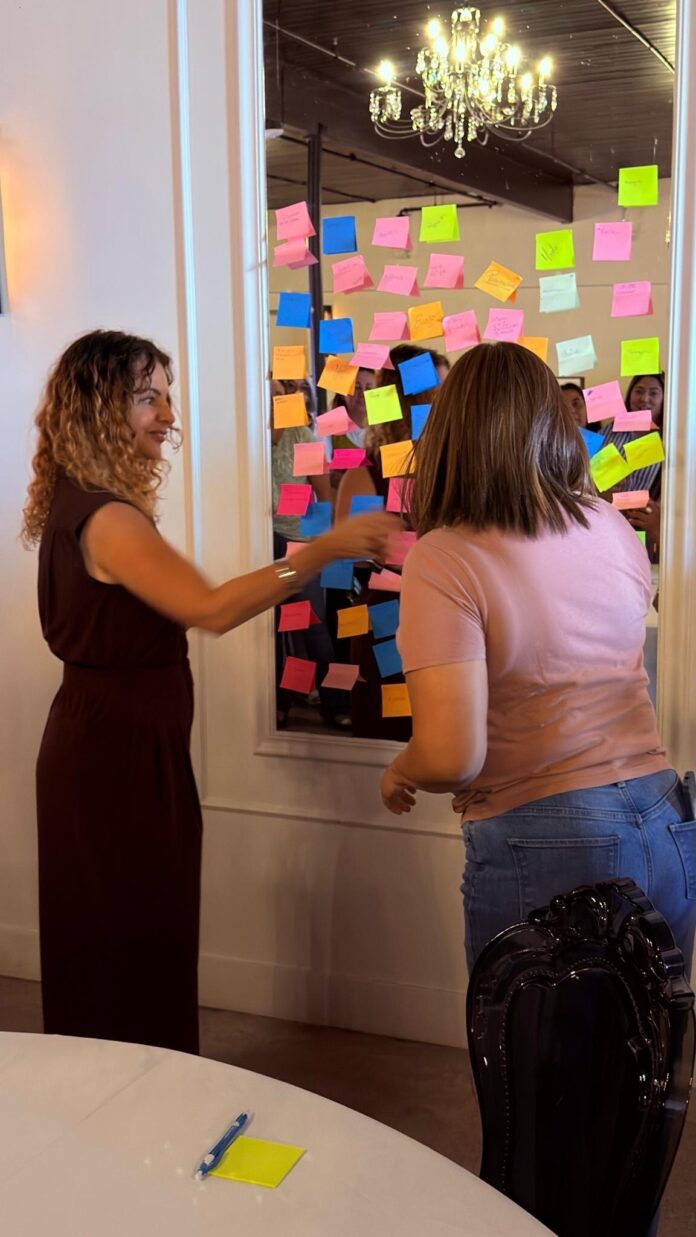 Laura Termini engaging the audience with an interactive “Sticky Notes” activity, inviting women to share messages of strength, humor, and solidarity.