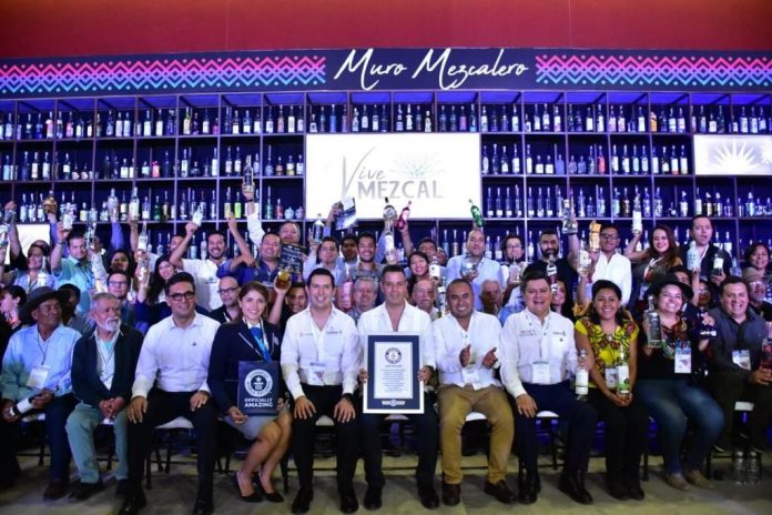 Mezcaleros and dignitaries were jubilant at the ceremony announcing Oaxaca’s win of the Guinness Record with the “Mezcal Wall” at Vive Mezcal, International Forum. In first row, center from left to right, starting with the Guinness representative: Natalia Ramirez, Guinness World Records, adjudicator; Juan Carlos Guzman Cobian, Oaxaca Secretary of the Economy; Alejandro Murat Hinojosa, Governor of Oaxaca; Dante Montano, Mayor Santa Lucia del Camino; and Juan Carlos Rivera Castellanos, Oaxaca Secretary of Tourism.